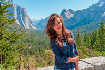 Naklejka premium A cute young woman walks through a green valley in Yosemite National Park with a view of the mountains