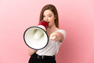 Teenager girl over isolated pink background shouting through a megaphone to announce something while pointing to the front