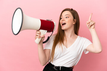 Teenager girl over isolated pink background shouting through a megaphone to announce something in lateral position