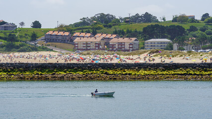 Obraz premium Aerial view of the beach in summer full of people and a small boat passing in front. Suances Santander.