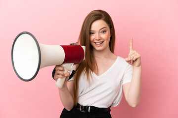 Teenager girl over isolated pink background holding a megaphone and pointing up a great idea