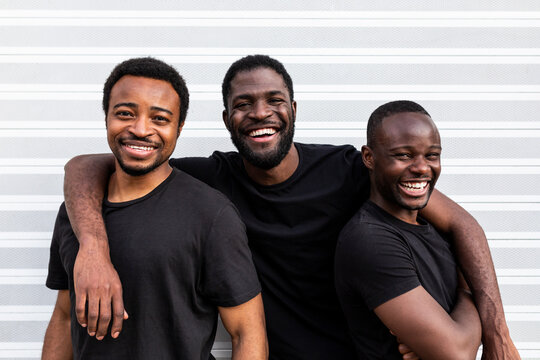 Cheerful black male friends embracing near striped wall