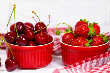 Juicy Fresh Strawberries and Sweet Cherry in a Red Bowls on piece of cloth on on a white Brick...