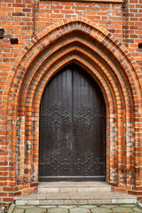 A gate in an orange brick building. Gothic architectural building. An old house with an iron gate to a museum or castle. Historical attraction.