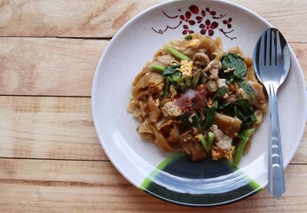 Stir-fried rice noodles, soy sauce with pork and kale in the dish, spoon and fork, Thai delicious food isolated on wooden background closeup.