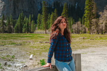 A cute young woman walks through a green valley in Yosemite National Park with a view of the mountains