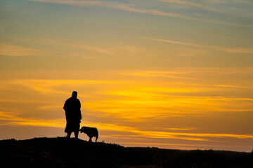 Fototapeta na wymiar Black and white silhouette of man and his dog on top of hill at sunset - room for text copy