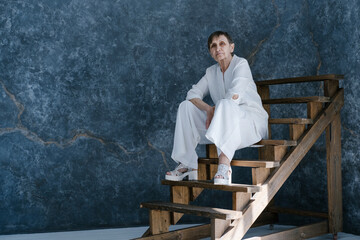 Studio portrait of beautiful looking old woman wearing white suit sitting on wooden stairs