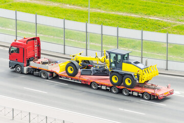 Grader tractor on transportation trailer truck with long trailer platform on the highway in the...