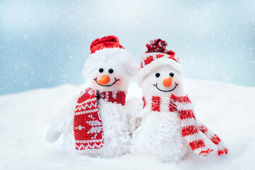 Merry Christmas and happy new year greeting card with copy space. Happy two little snowmen in cap and scarf standing in winter snow background. Christmas fairytale.