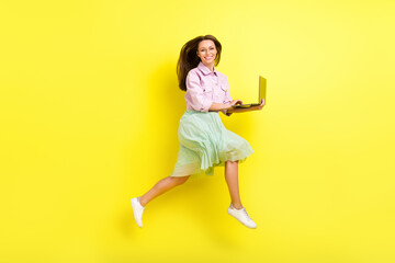 Full length body size view of attractive cheerful girl jumping using laptop running isolated over bright yellow color background