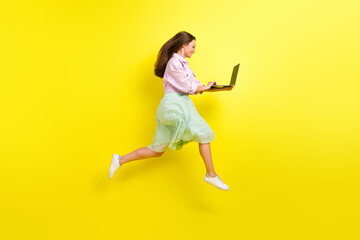 Fototapeta na wymiar Full length body size photo portrait girl in skirt jumping high working on computer isolated bright yellow color background
