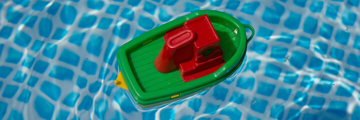 Small plastic toy boat floating in a swimming pool. Panoramic image