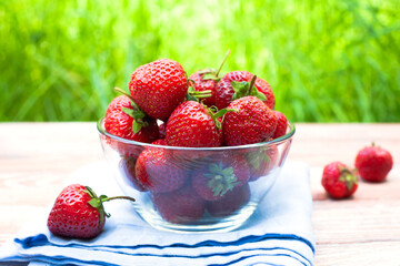 Ripe juicy strawberry in glass bowl on a wooden background. Close-up.