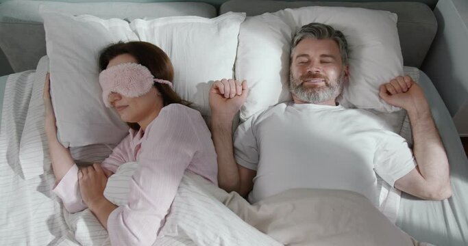 Mirthful man waking up at the bed and looking at his woman laying nearby. Man closed his ears because his wife is snorting at the morning. Relationships concept
