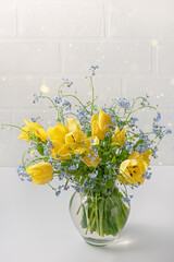 A bouquet of yellow tulips and blue flowers on a light background.