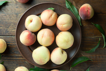 Ripe peaches in a clay plate on a wooden table with scattered leaves.