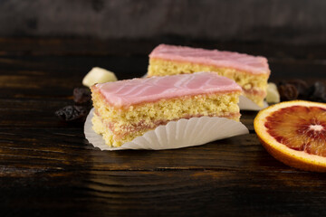 two sponge cakes in pink icing with a scattering of dried fruits with a slice of red orange