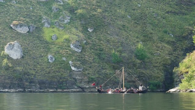Vikings Sail on an Old Ship Along a Quiet River Against the Backdrop of a Rocky Coast. The Men Row the Oars Diligently Towards Adventure. Medieval Reconstruction.