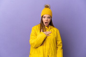 Teenager girl wearing a rainproof coat over isolated purple background surprised and shocked while looking right