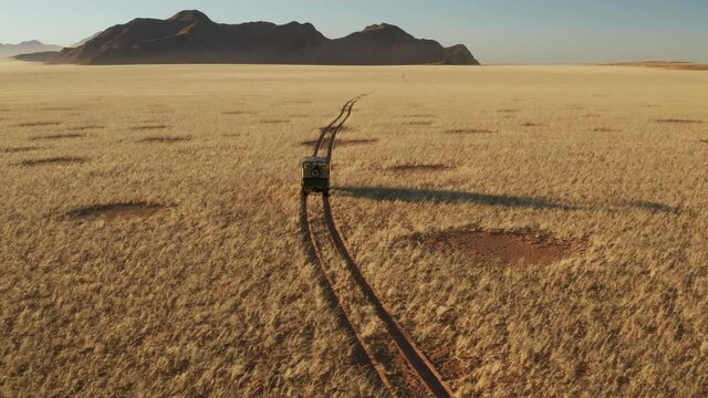 Spectacular epic tilt up aerial view of a safari vehicle driving through the grassy vegetation famous fairy circles in the Namib desert 