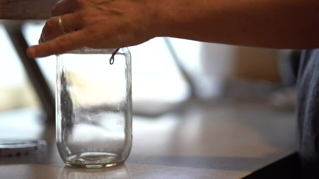 Quelqu'un prend un sachet de grains de caf&eacute; puis le verse dans un bocal en verre. 
