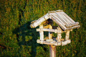 Wooden bird feeder in front of a green bush.