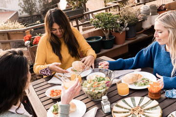 Happy multiracial friends eating breakfast in restaurant outdoors during coronavirus outbreak -...