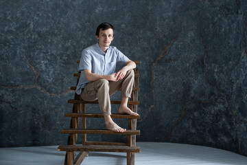 Studio portrait of young serious man wearing blue shirt sitting on wooden stairs
