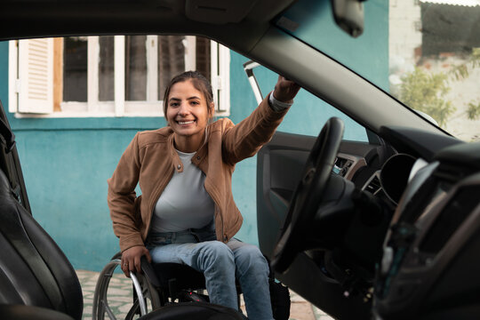 wheelchair woman in front of car and looking at camera.