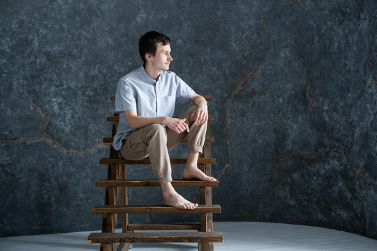 Studio portrait of young serious man wearing blue shirt sitting on wooden stairs