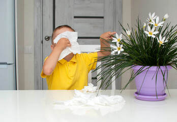Close-up of little boy blowing his nose in paper napkin at home next to flower. Allergic to flower...