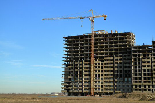 An image of a tower crane against the background of a house under construction.