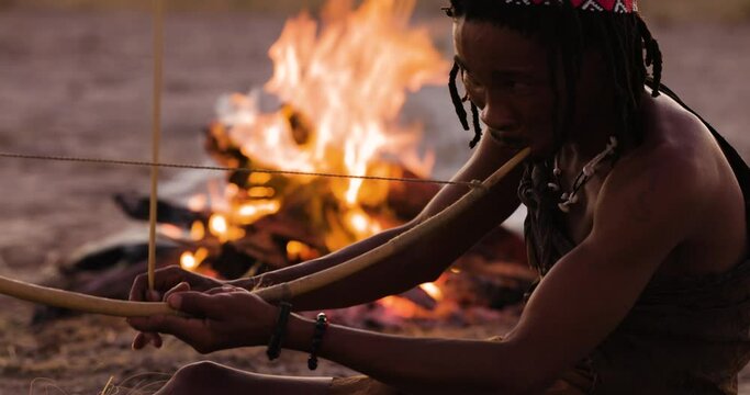 Close-up portrait view of San people (Bushmen)playing a traditional musical instrument at sunset around a fire