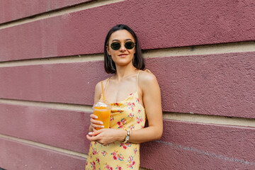 Adorable lovely modern girl in summer bright dress holding smoothie posing over pink wall and enjoy weekend