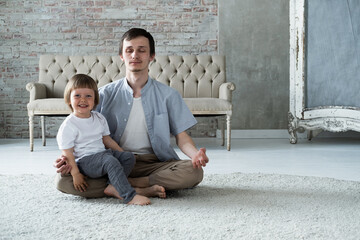 Young father trying to meditate sitting in lotus yoga pose with little son kid