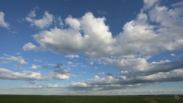 White clouds move across a blue sky above a prairie field in this time lapse.
