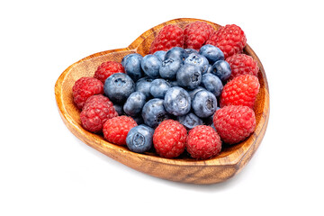 Raspberry and blueberry in wooden bowl in the shape of heart isolated on white background.