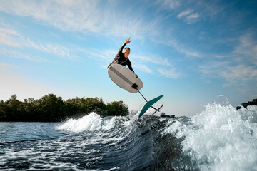 young athletic man vigorously jumping on the wave with foilboard