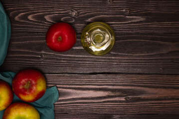 Apple cider vinegar in a glass decanter on a dark wooden table. Apples nearby. Top view, free space for text.