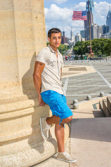 Dressing in a iron short sleeve shirt, blue shorts, a young attractive guy is standing by a column and looking at you.