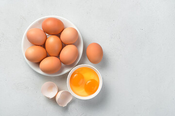 Raw chicken eggs and egg yolks on a gray concrete background.