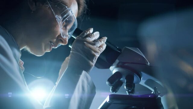 A woman scientist is looking into microscope, biochemical research. Scientific and medical lab instrument. A doctor is search for vaccine to treat diseases in laboratory for medicine study