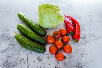 Organic vegetables for salad. Fresh tomatoes, red peppers, iceberg lettuce, cucumbers lie on a gray...