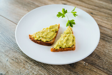 Avocado toasts with egg and shrimp on white plate on wooden table background
closeup.