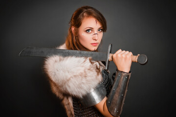 Medieval woman warrior in chain mail armor and polar fox fur on her shoulders standing with a sword...
