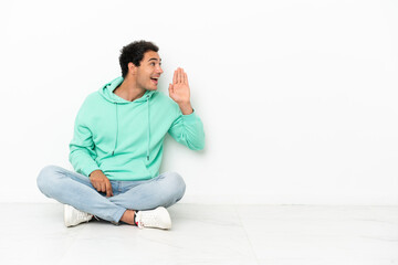 Caucasian handsome man sitting on the floor shouting with mouth wide open to the lateral