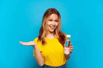 Teenager girl with a bottle of water over isolated blue background with shocked facial expression