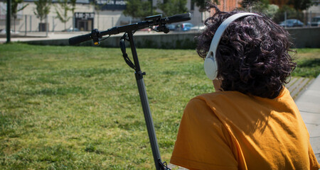 Woman In A Park Listening To Music With Headphones Next To An Electric Scooter.