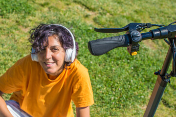 Woman In A Park Listening To Music With Headphones Next To An Electric Scooter.